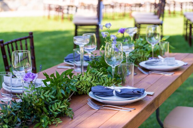 Beautifully decorated wooden table in a summer open-air cafe. Green branch and fresh flowers table decoration