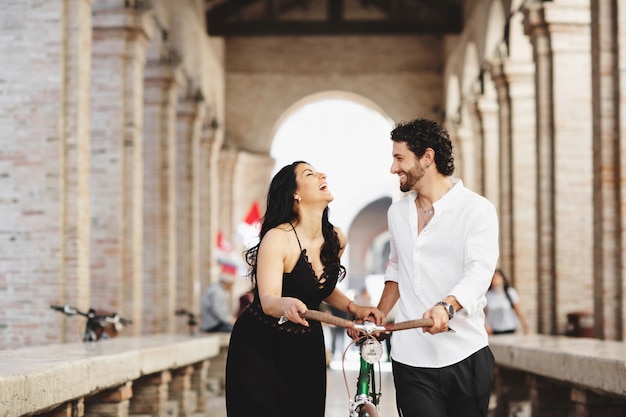 Beautifully dressed man and woman are walking in the old city with a bicycle