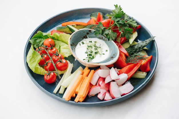 Beautifully plated variety of sliced and small vegetables over white background Sauce in the middle