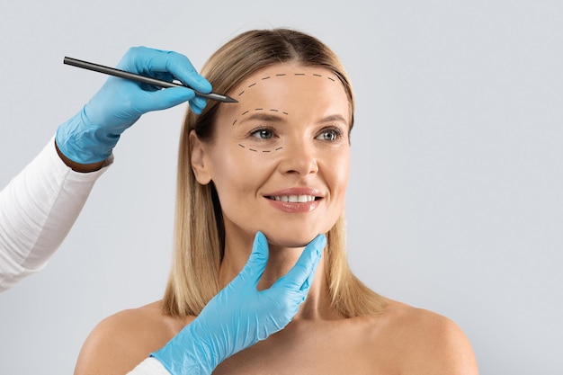 beautitian drawing contours on woman face before beauty treatment