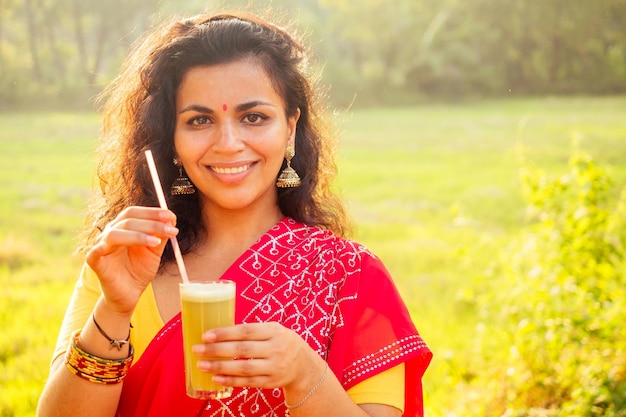 Beautuful induan woman in red sari standing near sugarcane juice maker apparatus machine plantation summer farm background small business start up