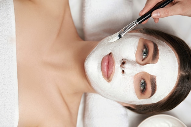 Bellezza. applicazione di maschera facciale bianca con pennello nel trattamento termale. spa per la cura della pelle e del corpo. trattamento di bellezza per il viso.