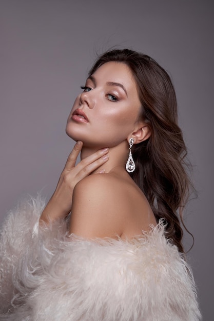 Beauty art portrait of a beautiful woman with long hair, white fur coat with long faux fur. Beautiful earrings in a woman's ears. Hairstyle, hair styling