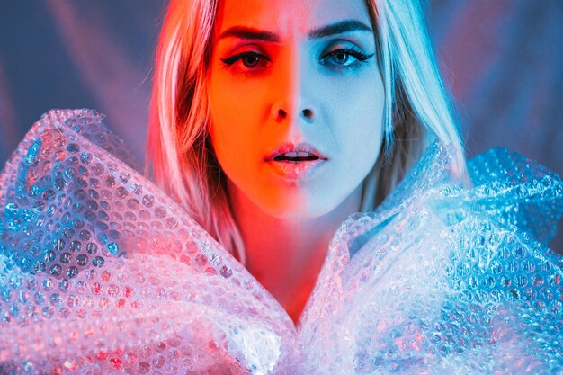 Beauty art portrait Plastic pollution Waste reuse Save planet Worried woman wrapping dress bubbles polyethylene film looking at camera blue pink neon light background