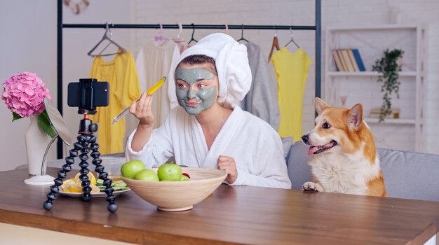 A Beauty Blogger in a White Robe with a White Towel on Her Head Applies a Green Moisturizing Mask to Her Face and Blogs about Skin Care and Cosmetics. Next Generation of Beauty Influencers