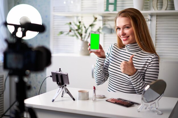 Photo beauty blogger woman filming advertising holding green screen smartphone application makeup influencer blonde girl live streaming cosmetics product review in studio asking for likes subscription