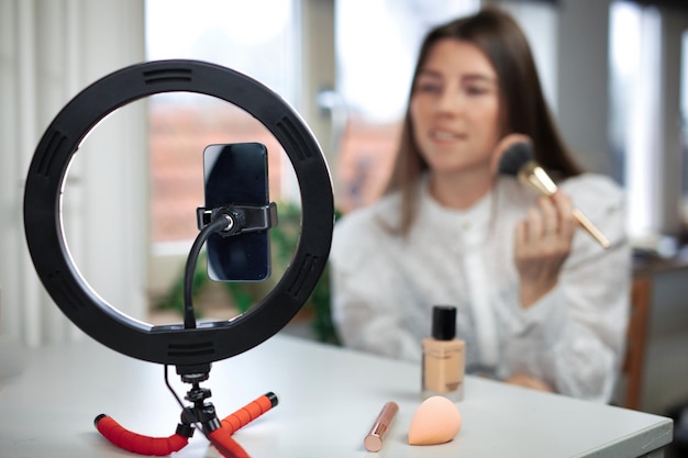 Beauty blogging technology and people concept portrait of a happy smiling girl blogger with ring light and smartphone applying make up at home making a influencer video
