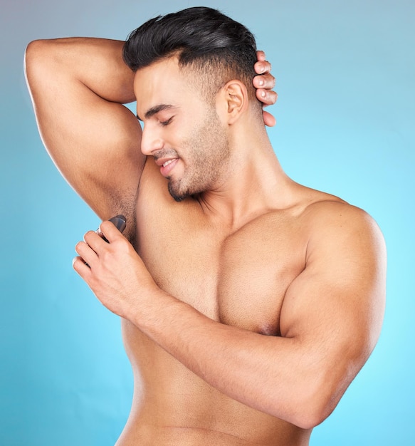 Beauty body and underarm with a man model applying antiperspirant to his armpit in studio on a blue background Product grooming and perfume with a male using roll on to smell fresh or clean