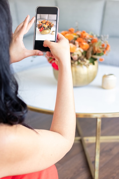 Beauty brunette woman is taking a photo of a cute floral bouquet inside a cabbage-painted pumpkin.