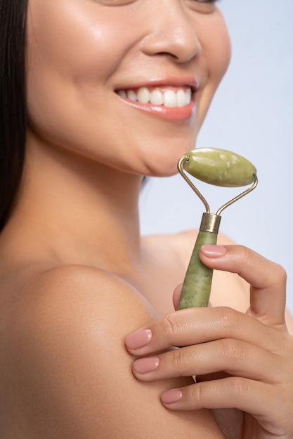 Beauty care. Pleased young woman keeping smile on her face, doing face massage