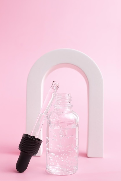 Сыворотка для лица коллагена красоты в стеклянной бутылке-капельнице в Арке на розовом фоне Модная съемка упаковки косметики Эфирное масло с натуральными ингредиентами