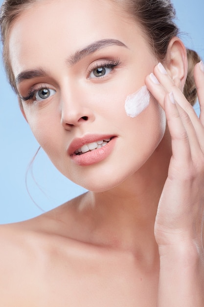 Concetto di bellezza, ritratto di bellezza di giovane donna che applica la crema sul viso. testa e spalle della donna naturalmente bella che tocca il fronte