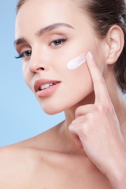 Beauty concept, beauty portrait of young woman applying cream on face, semi profile. Head and shoulders of naturally beautiful woman touching face