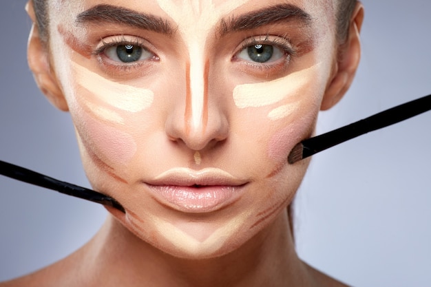 Photo beauty concept. closeup portrait of woman with contouring on face, doing make-up. types of drawing make-up, woman with nude make-up looking at camera, brushes near face