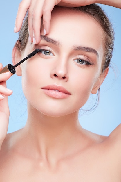 Beauty concept, head and shoulders of young woman with natural makeup. Closeup of girl looking at camera and painting lashes with mascara, applying mascara on eyelashes