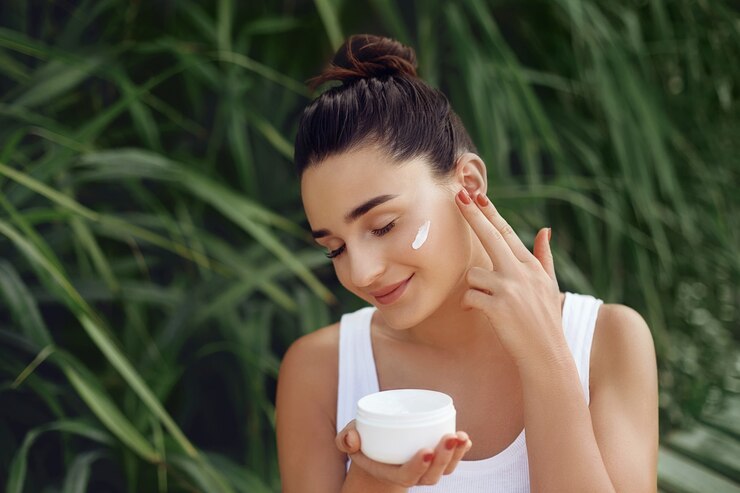 Beauty Concept. Portrait of Beautiful Woman Applying Cosmetics Cream on her face and Smiling. Body and Skin care