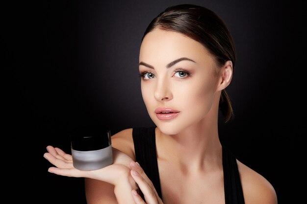 Beauty concept, woman looking at camera, cream staying on hand. Head and shoulders of beautiful young woman with smooth skin, selfcare. Studio, black background