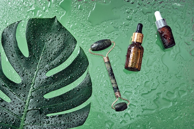 Beauty cosmetic lotion serum bottle and jade massage roller\
treatment skincare concept with monstera leaf and water drops\
background