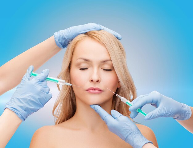 beauty and cosmetic surgery concept - woman with closed eyes and beautician hands with syringes