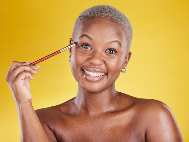 Beauty cosmetics and portrait of black woman with brush in hand in studio and skincare isolated on yellow background happy makeup routine eye shadow and smile face of model with luxury product