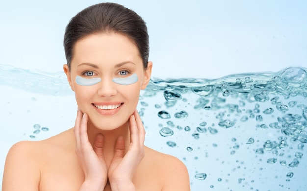 beauty, cosmetology, hydration, people and rejuvenation concept - beautiful young woman face with hydrogel under-eye patches over blue background and water bubbles