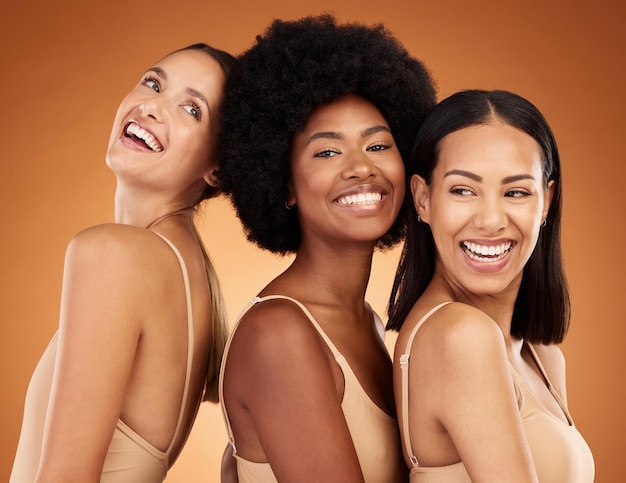 Beauty diversity and skincare with woman friends in studio on an orange or brown background Happy natural and real with a different female group posing together for wellness or skin health