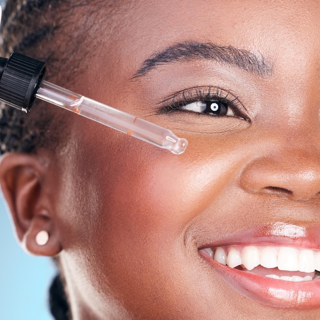 Beauty face and happy black woman with serum skin hydration anti aging or collagen oil for studio skincare treatment Retinol dropper hyaluronic acid or closeup African person on blue background