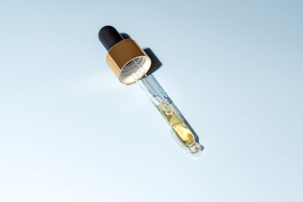 beauty face oil dripping from gold dropper on blue background skin care cosmetic advertisement with copy space