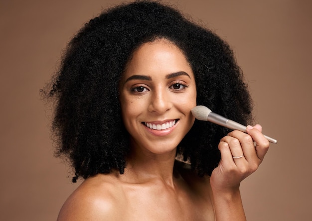 Beauty face portrait and black woman with makeup brush in studio isolated on a brown background Cosmetics tool skincare and happy female model with product to apply foundation for facial wellness