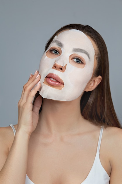 Cura della pelle del viso di bellezza. la donna applica una maschera idratante in panno sul viso. modello di ragazza con maschera cosmetica. trattamento facciale