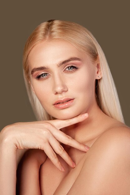 Beauty face Skin rejuvenation Blonde woman with natural makeup bare skin hand at chin isolated on brown