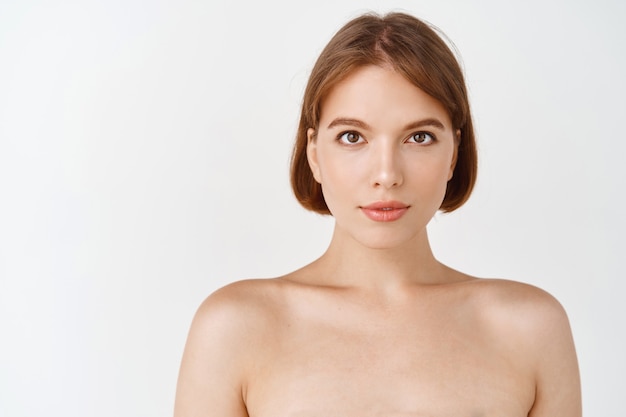 Volto di bellezza. ragazza con le spalle nude e lo sguardo naturale di trucco facciale. donna con pelle fresca e pulita, cosmetici per la cura della pelle dopo l'effetto, muro bianco