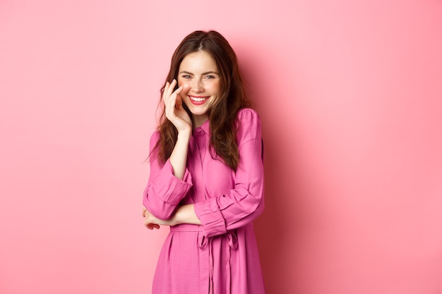 Beauty and fashion. Attractive caucasian woman giggle and smile at camera, posing in romantic bright dress on fine spring day, standing against pink wall.