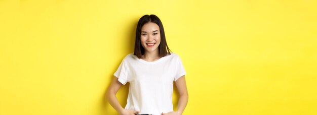 Beauty and fashion concept stylish asian girl in white tshirt smiling happy and standing over yellow