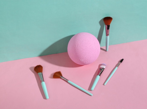 Beauty and fashion minimalistic scene Makeup brushes with ball on blue pink pastel background with trendy shadows Creative layout