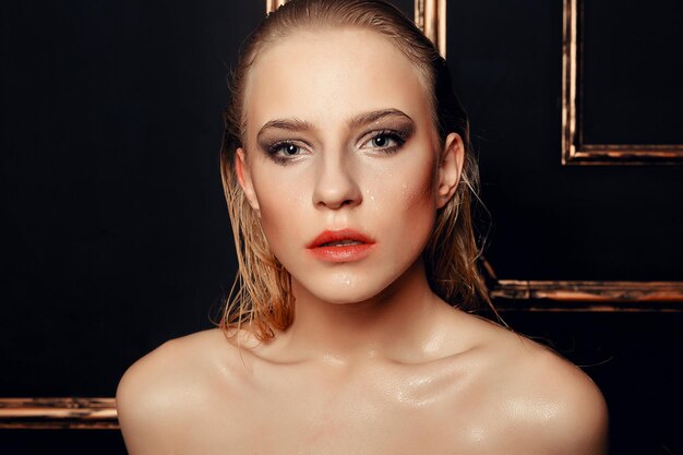 Beauty fashion model girl natural makeup wet hair on black gold background in warm tones. Portrait of young woman with fashion makeup