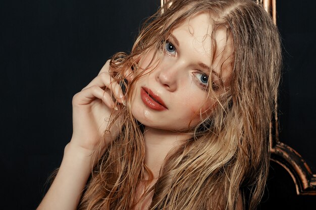 Beauty fashion model girl natural makeup wet hair on black gold background in warm tones. Portrait of young woman with fashion makeup