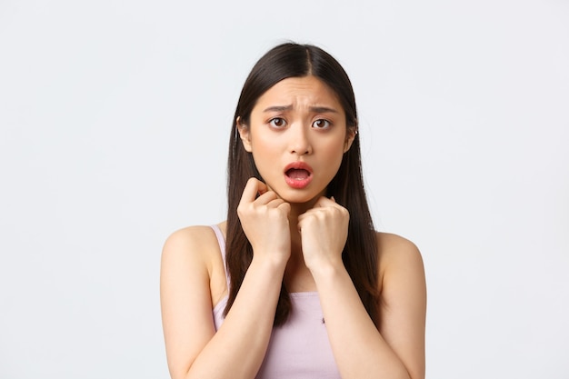 Beauty, fashion and people emotions concept. Close-up portrait of concerned and scared, timid asian girl, hold hands pressed to chest, gasping afraid