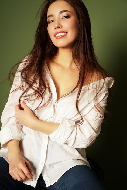 Портрет моды красоты усмехаясь сексуальной чувственной азиатской молодой женщины с темными длинными волосами в белой рубашке