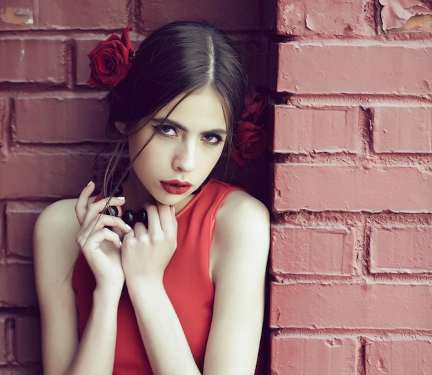 Beauty and fashion spanish woman with fashionable makeup and rose flower in hair girl in red dress on brick wall background