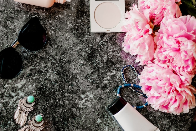 Beauty flat lay with accessories, perfume, cosmetics and peonies on a dark marble background