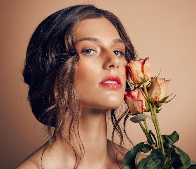 Beauty flowers and face of woman in studio for wellness fashion and skincare on brown background Makeup cosmetics and female model with roses for beauty salon natural self care and spa aesthetic