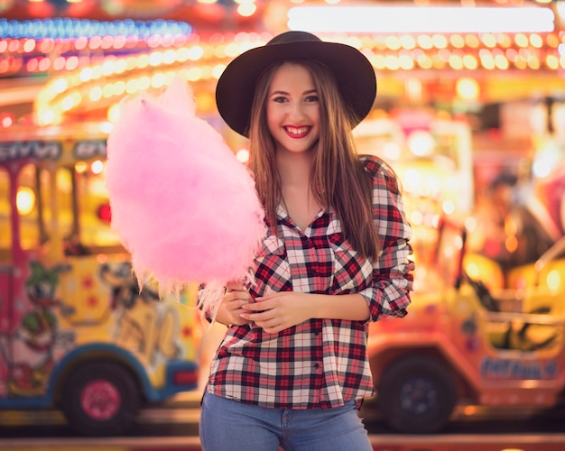 Photo beauty girl with a cotton candy in a fair with many lights