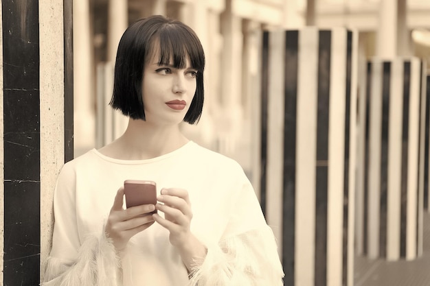 パリフランスのセクシーな表情を持つ美少女 赤い唇を持つ女性はスマートフォンで使用します ブルネットの髪を持つ女性は携帯電話を保持します モバイルデバイスを持つファッションモデル 現代生活のための新技術