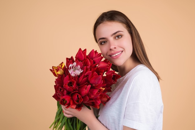 チューリップを持つ美しさの少女美しい官能的な女性は、ベージュの背景にチューリップのスタジオ ポートレートの花束を保持します
