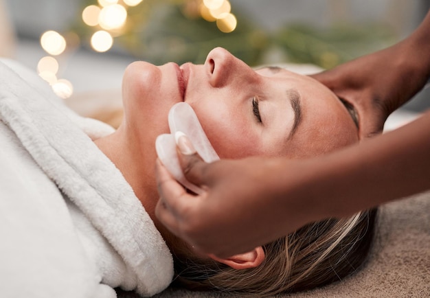 Beauty gua sha and woman getting a facial massage for wellness health and self care at a spa Skincare cosmetic and calm young female doing a luxury face treatment with rose quartz at a zen salon