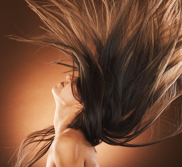 Photo beauty hair and freedom with a model woman in studio on a brown background for strong haircare wellness luxury and salon with an attractive young female hair flick to promote a keratin product