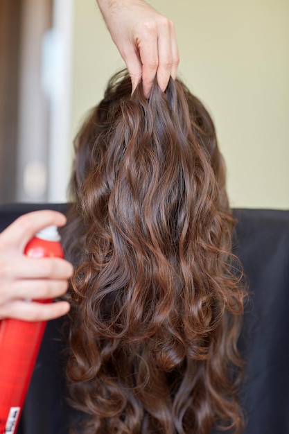 beauty, hairstyle and people concept - closeup of woman head and stylist hands with hair spray making hairdo at salon