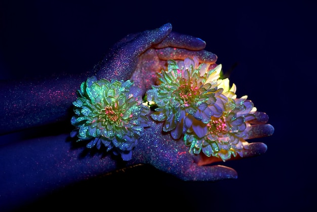 Beauty hands of a woman in ultraviolet light with flowers in the palms. Cosmetics for hand skin care