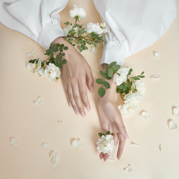 バラの花を持つ美の手の女性がテーブルの上にあります。ハンドスキンケア用の天然化粧品。ファッションメイク